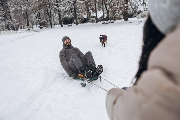 Photo un jeune couple avec un chien qui s'amuse à faire du traîneau en tirant un traîneau en hiver pendant la saison enneigée