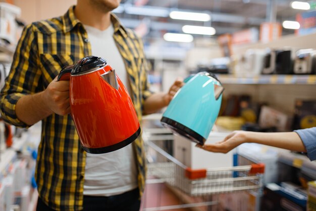 Jeune couple choisissant une bouilloire électrique dans un magasin d'électronique. Homme et femme achetant des appareils électriques ménagers sur le marché