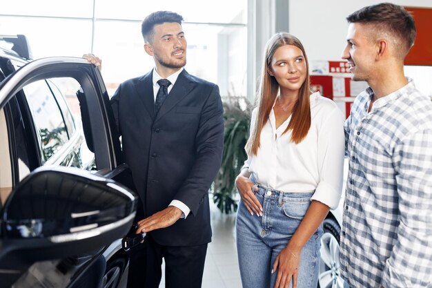 Photo jeune couple choisissant une voiture chez le concessionnaire avec l'aide du gestionnaire