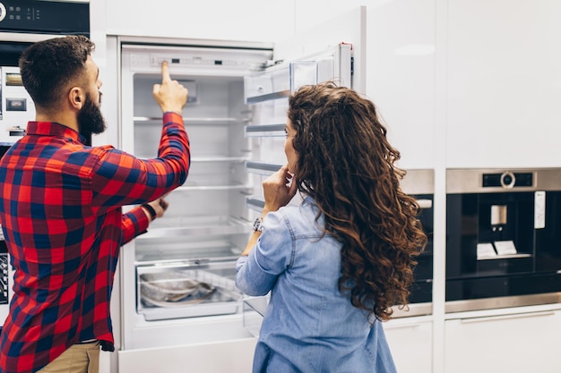 Jeune couple, clients satisfaits choisissant un réfrigérateur dans un magasin d'électroménagers.