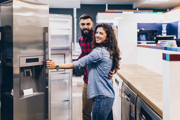 Jeune couple, clients satisfaits choisissant un réfrigérateur dans un magasin d'électroménagers.