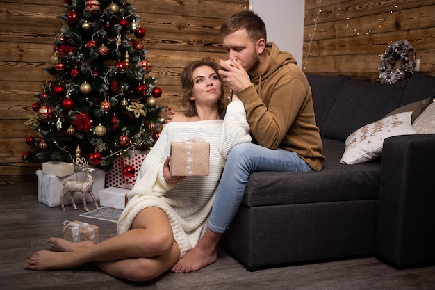 Jeune couple avec coffret cadeau profitant de leur temps ensemble à la maison. Arbre de Noël sur fond.