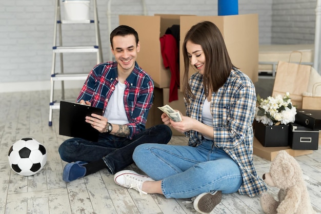 Jeune couple comptant de l'argent assis sur le sol dans un nouvel appartement