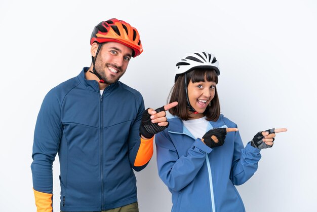 Jeune couple cycliste isolé sur fond blanc pointant le doigt sur le côté en position latérale