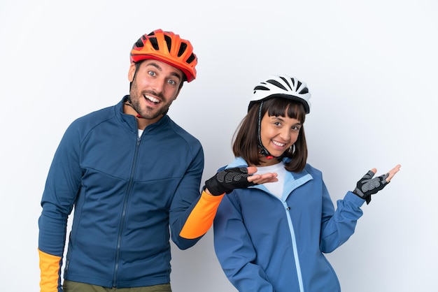 Jeune couple cycliste isolé sur fond blanc pointant vers l'arrière et présentant un produit