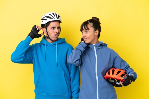 Jeune couple cycliste isolé sur fond jaune ayant des doutes en se grattant la tête