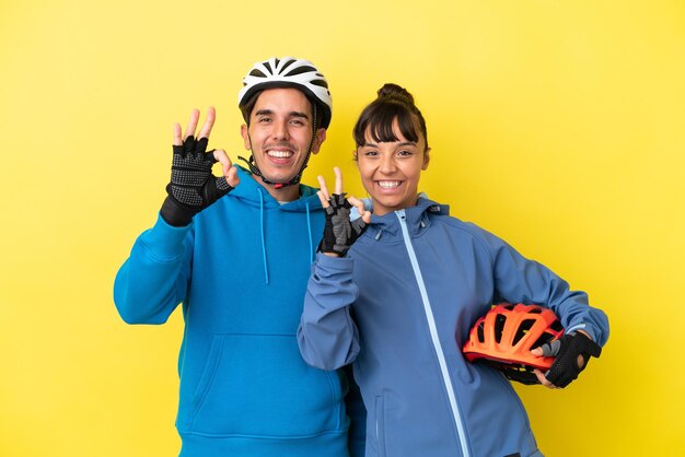 Jeune couple cycliste isolé sur fond jaune montrant un signe ok avec les doigts