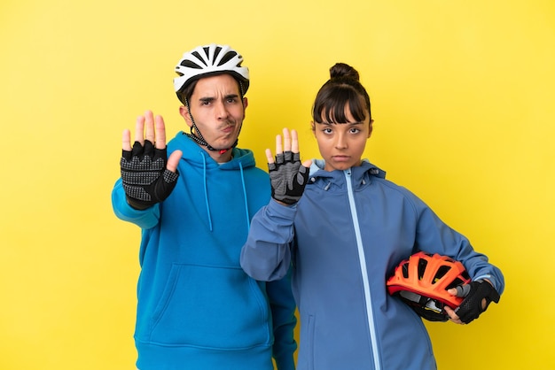 Jeune couple de cyclistes isolé sur fond jaune faisant un geste d'arrêt niant une situation qui pense mal