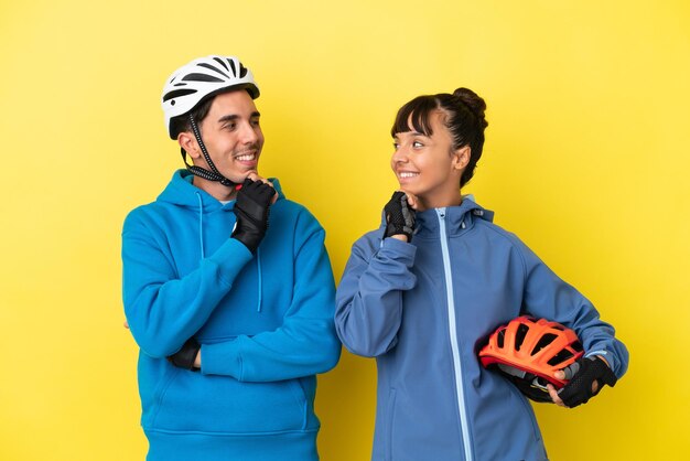 Jeune couple de cyclistes isolé sur fond jaune regardant les uns les autres