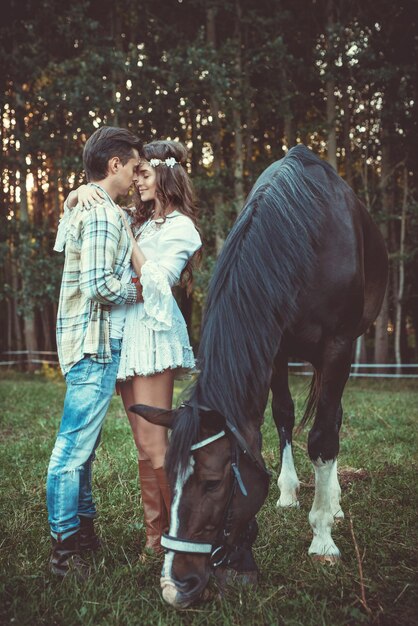 Photo un jeune couple dans les bras sur le pré avec un cheval.