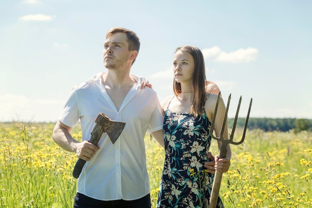 Jeune couple dans un champ dans un village par une journée d'été ensoleillée Un gars avec une hache une fille avec une fourche Grands loisirs de plein air