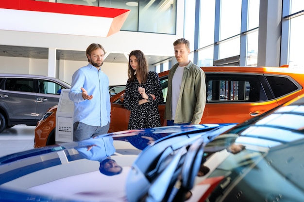 Photo un jeune couple dans une concession automobile un employé de la concession automobile aide à la sélection un achat coûteux