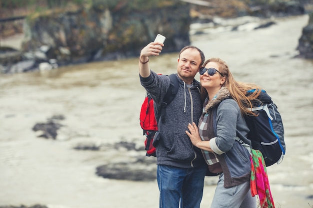 Jeune couple dans les montagnes avec des sacs à dos au printemps fait un selfie