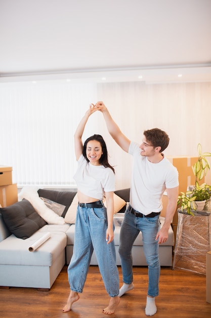 Jeune couple dansant dans le salon près de boîtes en carton divertissant le jour du déménagement, mari et femme heureux s'amusent à tourbillonner en se déplaçant ensemble dans leur propre appartement.