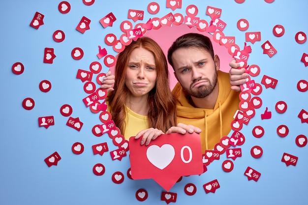 jeune couple debout avec une expression faciale bouleversée n'ayant pas de taux et aime les signes sur les publications et les photos