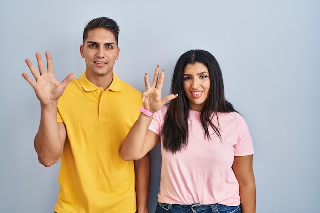 Jeune couple debout sur fond isolé montrant et pointant vers le haut avec les doigts numéro neuf tout en souriant confiant et heureux.