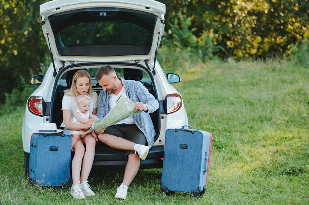 Jeune couple debout près du coffre de voiture ouvert avec des valises, regardant la caméra, à l'extérieur