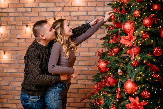 Jeune couple décorant l'arbre de noël ensemble à la maison