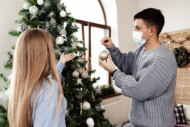 Jeune couple, décoration, arbre noël, chez soi, porter, masques visage, gros plan