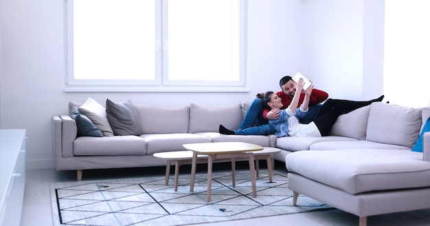 Jeune couple de détente dans une maison luxueuse avec des tableaux informatiques dans le salon sur le canapé-lit.