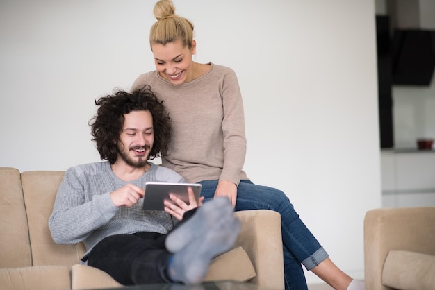 Jeune couple de détente dans une maison luxueuse avec des tableaux informatiques dans le salon sur le canapé-lit.