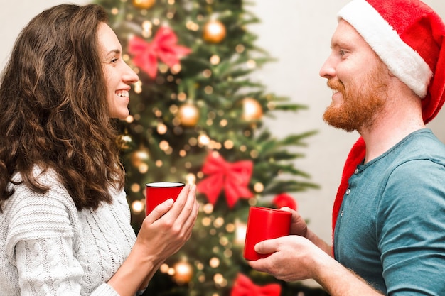 Un jeune couple avec du thé chaud dans les mains communique sur le fond de l'arbre de Noël