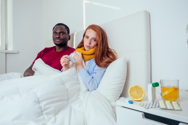 Jeune couple en écharpe tricotée dans la chambre, malade et mesure la température.