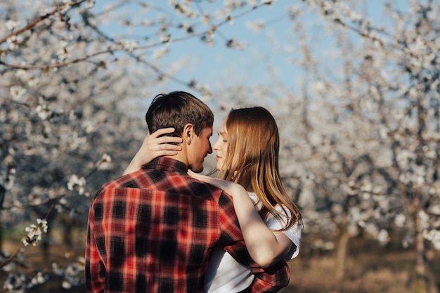 Jeune couple élégant étreint près des arbres de fleurs de printemps.