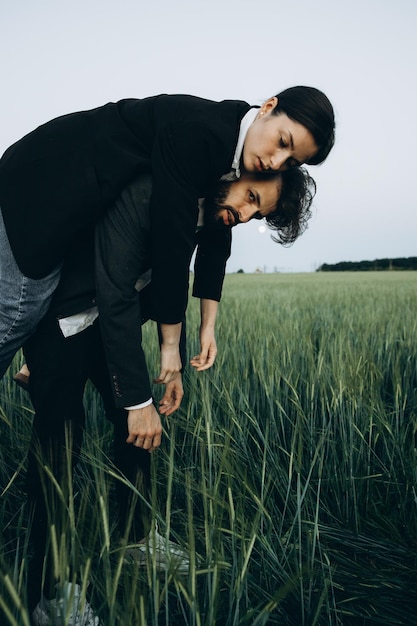 Jeune couple élégant de mari et femme vêtus de costumes classiques lors d'une séance photo au milieu d'un champ vert Le concept de la relation entre un couple de personnes amoureuses