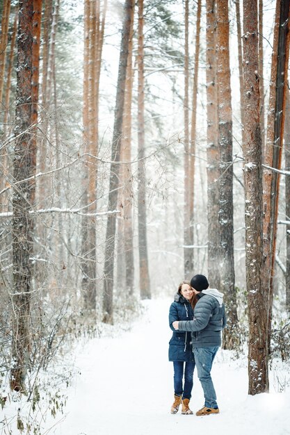 Jeune couple embrassant dans la forêt d'hiver. Vacances d'hiver. Une escapade le temps d'un week-end. Espace pour le texte. Couleurs naturelles, mise au point sélective.