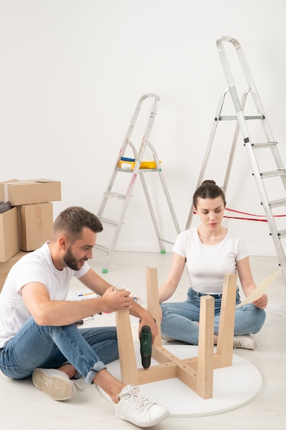 Jeune couple emménageant dans une nouvelle maison assis sur le sol et assembler une table basse ensemble