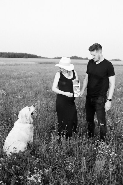 Un jeune couple enceinte montre une échographie de l'enfant à naître à son chien en promenade le soir d'été. Photo en noir et blanc. En attente d'enfant. Gestion de la grossesse. Méthodes modernes d'examen.