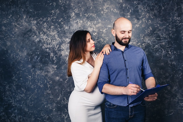 Jeune couple enceinte avec un presse-papiers dans leurs mains.