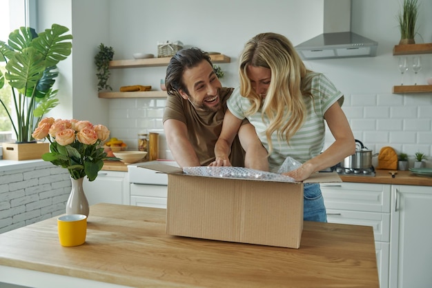 Un jeune couple enjoué déballe une boîte alors qu'ils se tiennent à la cuisine domestique