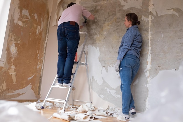 Jeune couple enlevant le vieux papier peint des murs se préparant à la rénovation d'un appartement