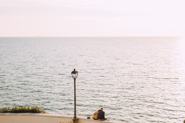 Un jeune couple est assis l'un à côté de l'autre et regarde la mer.