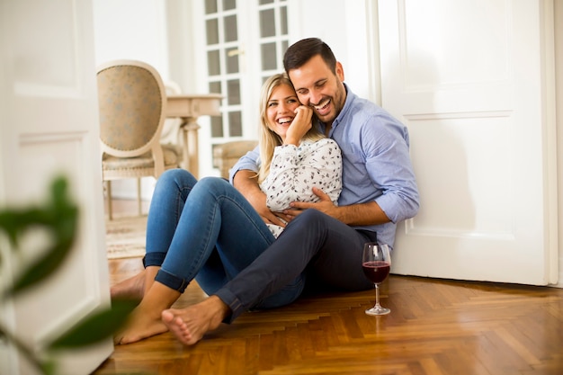 Jeune couple est assis sur le sol, boire du vin rouge et une femme à l&#39;aide de téléphone portable à la maison