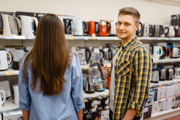 Jeune couple à l'étagère avec des bouilloires électriques dans un magasin d'électronique. Homme et femme achetant des appareils électriques ménagers sur le marché