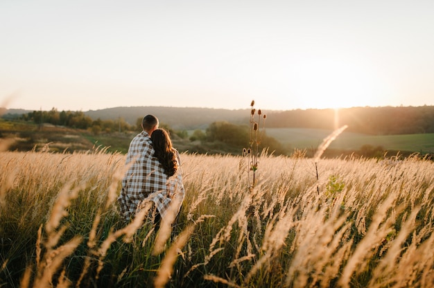 Jeune couple étreignant, debout en arrière, les gens recouverts d'une couverture, au coucher du soleil à l'automne un extérieur. Concept de famille sympathique.