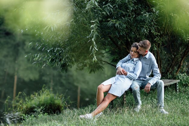 Photo jeune couple étreint et assis près du lac par une journée ensoleillée.