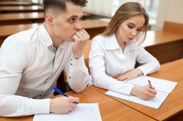 Jeune couple d'étudiants, un gars et une fille, s'asseoir à un bureau lors d'une conférence et se tenir la main