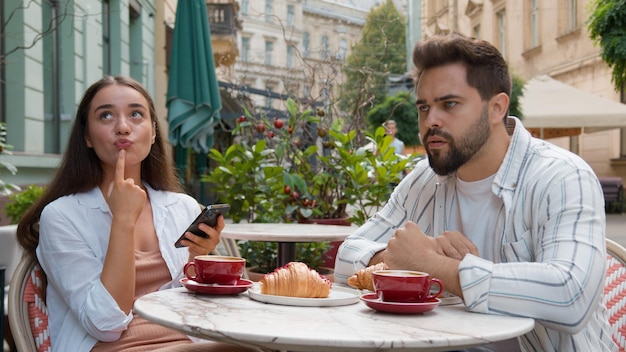 Un jeune couple européen dans un café de la ville femme souriante rire SMS émotionnel smartphone ignorer l'homme