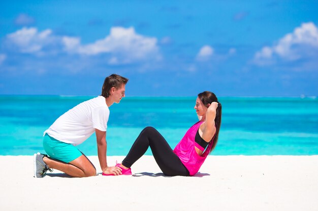 Jeune couple faire des abdominaux crunches sur une plage blanche pendant les vacances
