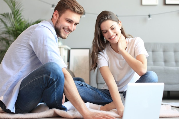 Jeune couple faisant des achats en ligne à la maison, à l'aide d'un ordinateur portable au sol.