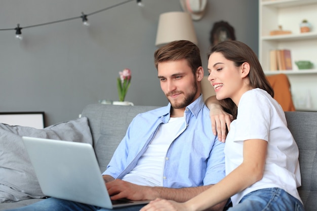 Jeune couple faisant des achats en ligne à la maison, à l'aide d'un ordinateur portable sur le canapé.