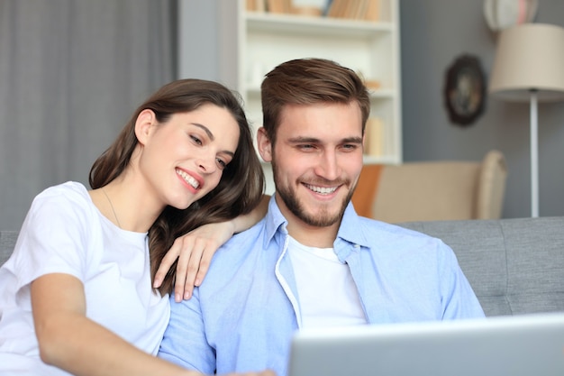 Jeune couple faisant des achats en ligne à la maison, à l'aide d'un ordinateur portable sur le canapé.