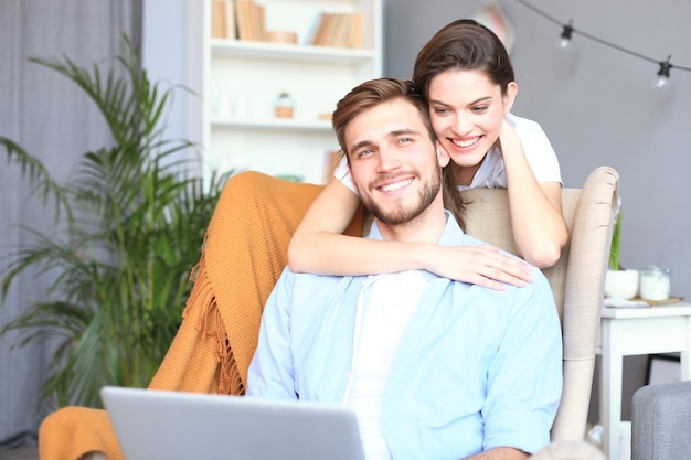 Jeune couple faisant des achats en ligne à la maison, à l'aide d'un ordinateur portable sur le canapé.