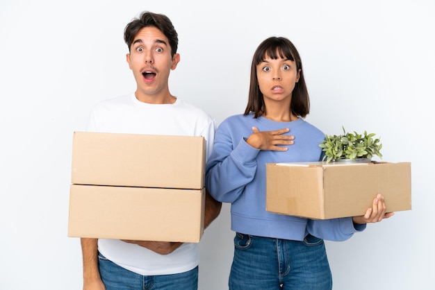 Jeune couple faisant un geste tout en ramassant une boîte pleine de choses isolées sur fond blanc avec une expression faciale surprise et choquée