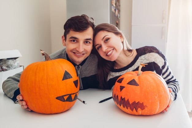 Jeune couple faisant jack-o-lanterne pour halloween dans la cuisine. Heureux homme et femme préparent des citrouilles pour les vacances