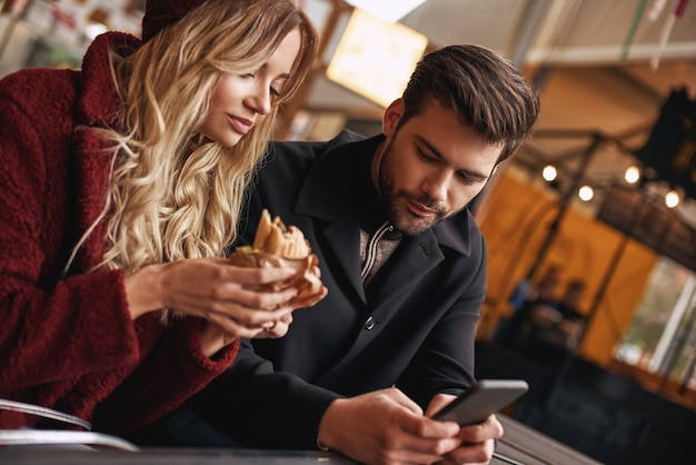 Un jeune couple fait des selfies tenant des sandwichs au marché de l'alimentation de rue